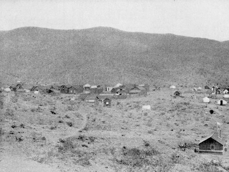 Black and white view of the White Hills mining camp in the 1890s, with buildings spread across the desert below the hills